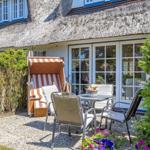 Haus mit Strohdach, Terrasse mit Tisch, Stühlen und Strandkorb.