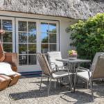 Terrasse mit Sitzgruppe, Strandkorb und Blumen vor einem Haus mit Strohdach.