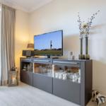 TV auf grauem Sideboard, Fenster mit Blick auf Garten, Dekoration mit Vasen und Kuhfiguren.