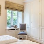 Bedroom with white bed, window, chair, and wardrobe.