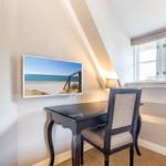 Desk with chair under sloped ceiling and window. Wall picture shows beach.