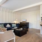 Living room with fireplace, sofa and chairs. Wooden floor and white walls.