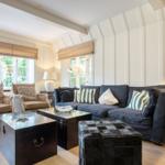 Living room with sofa, two armchairs, tables, and windows.