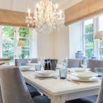 Dining room with table, chairs, and chandelier. Windows overlooking garden.
