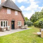 Red brick house with thatched roof, terrace, and garden with lounge chairs.