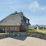Haus mit Strohdach, Steinmauer und Blick aufs Meer.