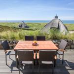 Terrasse mit Tisch und Stühlen, Blick auf Strand und Dachhäuser.