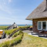 Haus mit Dach aus Stroh, Terrasse mit Liegen und Blick auf das Meer.
