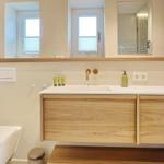 Bad mit Waschbecken, Spiegel und Toilette. Holzunterschrank und Fenster.