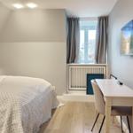 Schlafzimmer mit Bett, Schreibtisch und Fernseher an der Wand.
