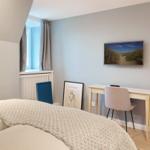 Schlafzimmer mit Bett, Schreibtisch und Wandbild.