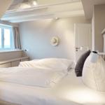 Schlafzimmer mit Dachschrägen, Fenster und Bett mit weißen Laken.