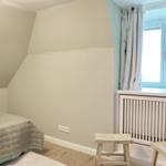 Zimmer mit Bett, Fenster und Holzmöbeln. Dachschrägen und weiße Wände.