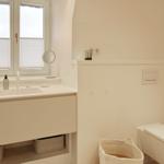 Badezimmer mit Waschbecken, Spiegel und Toilette. Fenster mit Jalousie.