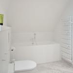 Bad mit Badewanne, Toilette und Dusche. Drei grüne Flaschen auf dem Waschtisch.