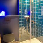 Badezimmer mit Dusche, Toilette und Neonlicht.