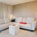 Ein Wohnzimmer mit einem hellen Ecksofa, einem Koffer-Tisch und hängenden Lampen.