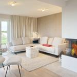 Wohnzimmer mit Sofa, Kamin und Blick auf Grünfläche.