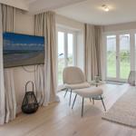 Wohnzimmer mit Fernseher, Sitzgelegenheiten und Blick auf Grünflächen.