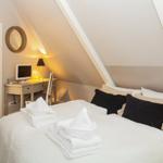 Schlafzimmer mit Dachschräge, Bett mit Kissen und Handtüchern, Schreibtisch mit Monitor und Lampe.