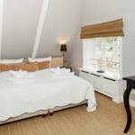 Schlafzimmer mit Doppelbett, zwei Nachttischen und Schreibtisch. Fenster mit Rollladen und Wandlampe.