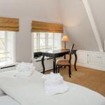 Schlafzimmer mit Dachschräge, zwei Fenstern, Schreibtisch und Bett mit Handtüchern.