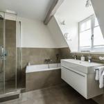 Bathroom with shower, bathtub, and sink under sloped ceiling.