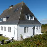 White house with gray roof, garden with lounge chairs and flower beds.