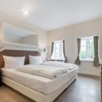 Schlafzimmer mit Doppelbett, Fenstern und Fernseher.