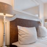 Schlafzimmer mit Bett, Kopfteil und Stehlampe. Fenster mit Vorhang.