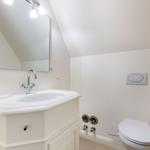 Badezimmer mit Waschbecken, Spiegel und Toilette unter Dachschrägen.