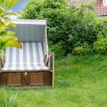 Hochbeet mit Streifenbezug im Garten. Hintergrund: grüne Hecke und Haus.