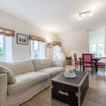Wohn- und Essbereich mit Sofa, Tisch und Stühlen. Holzboden und große Fenster.