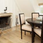Dining room with round table, striped chairs, and fireplace with wood.