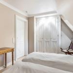 Schlafzimmer mit Bett, Schrank und Holzstuhl unter Dachschrägen.