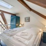 Schlafzimmer mit Dachschrägen, Bett, Kleiderschrank und Tischlampen.