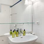 Badezimmer mit Waschbecken, Spiegel und grünen Flaschen.