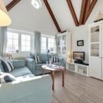 Wohnzimmer mit hellblauen Sofas, Holzboden und weißen Schränken unter hohem Dach.