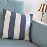 Ein Kissen mit Streifen liegt auf einem Sofa. Eine Stehlampe steht daneben.