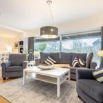 Wohnzimmer mit grauem Sofa, weißen Möbeln und großem Fenster.