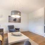 Wohnzimmer mit Sofa, Sessel, Couchtisch und Fernseher an der Wand.