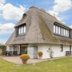 Haus mit strohgedecktem Dach, Terrasse und Garten.
