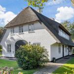House with thatched roof, white walls, and garden. Inviting atmosphere with seating area.