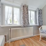 Room with bed, windows, radiator, and chair with cushion.