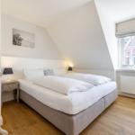 Schlafzimmer mit Doppelbett, Holzboden und Fenster mit Blick auf Gebäude.