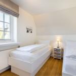 Zwei Einzelbetten, Fenster, Nachttisch mit Lampe und Holzboden.