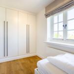 Schlafzimmer mit weißem Schrank, Holzboden und Fenster mit Blick nach draußen.