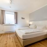 Schlafzimmer mit Doppelbett, Holzboden und Fenster mit Vorhängen.