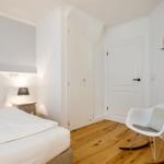 Schlafzimmer mit Bett, Nachttisch, Stuhl und runden Spiegel an der Wand.