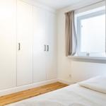 Schlafzimmer mit weißem Schrank, Holzboden und Fenster mit Vorhängen.